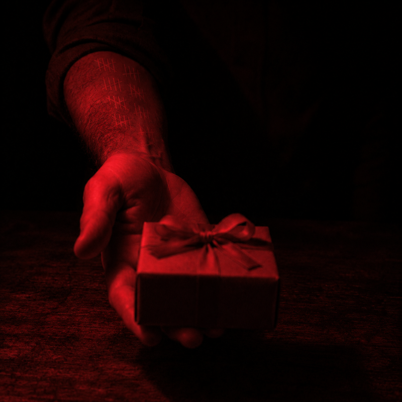 Covert contract psychology: a hand offering a wrapped gift across a dark table, faint tally marks counted up the giver’s own forearm