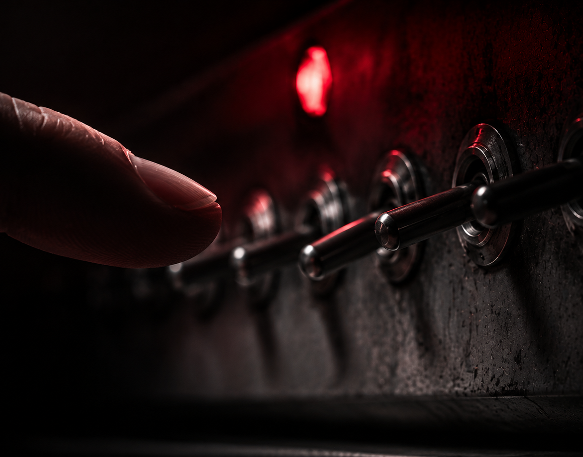 The Milgram experiment: a fingertip hovering over one toggle switch on a worn vintage instrument panel, the rest of the row falling into shadow
